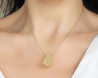 Puede incluir: Un collar de cadena dorada con un colgante de color amarillo claro de forma irregular.