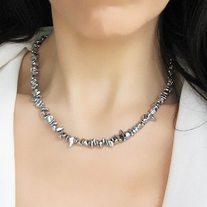 Könnte beinhalten: Eine silberne Halskette mit einem gezackten, unregelmäßigen Design. Die Halskette besteht aus kleinen, spitzen Metallteilen, die miteinander verbunden sind.