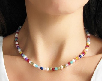 May include: A colorful beaded necklace with a variety of stones and pearls. The necklace is made of small, round beads in shades of red, orange, yellow, green, blue, purple, and white.
