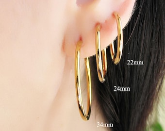 Op de afbeelding: Goudkleurige oorringen in drie maten: 22 mm, 24 mm en 34 mm. De oorbellen worden op een oor gedragen en tonen hun verschillende maten en een glanzende, gepolijste afwerking. De oorbellen hebben een eenvoudig, elegant ontwerp.