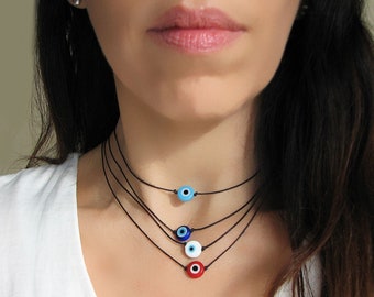Puede incluir: Un collar de capas con cuatro cordones negros y cuatro amuletos de ojo turco de diferentes colores. Los amuletos son azules, azul claro, blancos y rojos.