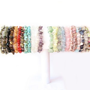 Pode incluir: Um expositor de 18 pulseiras de lascas coloridas feitas de várias pedras naturais, incluindo turquesa, ametista, quartzo rosa e olho de tigre.
