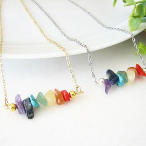 Peut inclure: Trois colliers avec des éclats de pierres précieuses arc-en-ciel. Les colliers sont sur une surface blanche. Les colliers sont en or, en argent et en or.