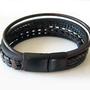 May include: A multi-layered leather bracelet with a black braided leather strap and a black metal clasp.