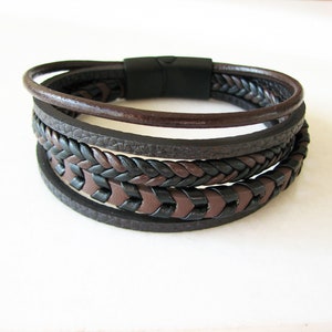 May include: A multi-layered leather bracelet with a braided design in black and brown. The bracelet has a magnetic clasp.