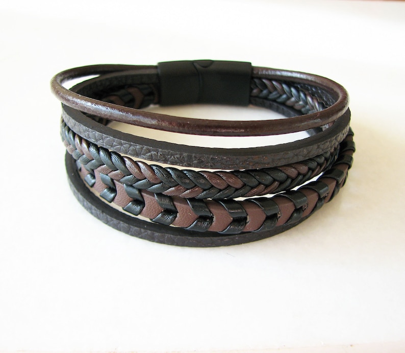 May include: A multi-layered leather bracelet with a braided design in black and brown. The bracelet has a magnetic clasp.
