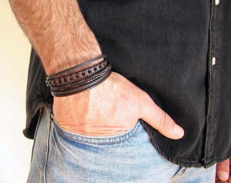 May include: A brown leather bracelet with multiple braided and woven straps. The bracelet is worn on a person's wrist.