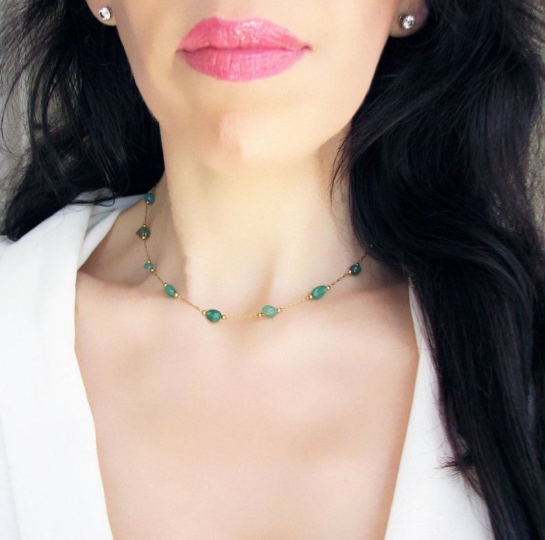 Puede incluir: Un delicado collar de cadena de oro con peque&ntilde;as piedras preciosas verdes de forma ovalada. El collar lo lleva una persona con el pelo largo y negro.