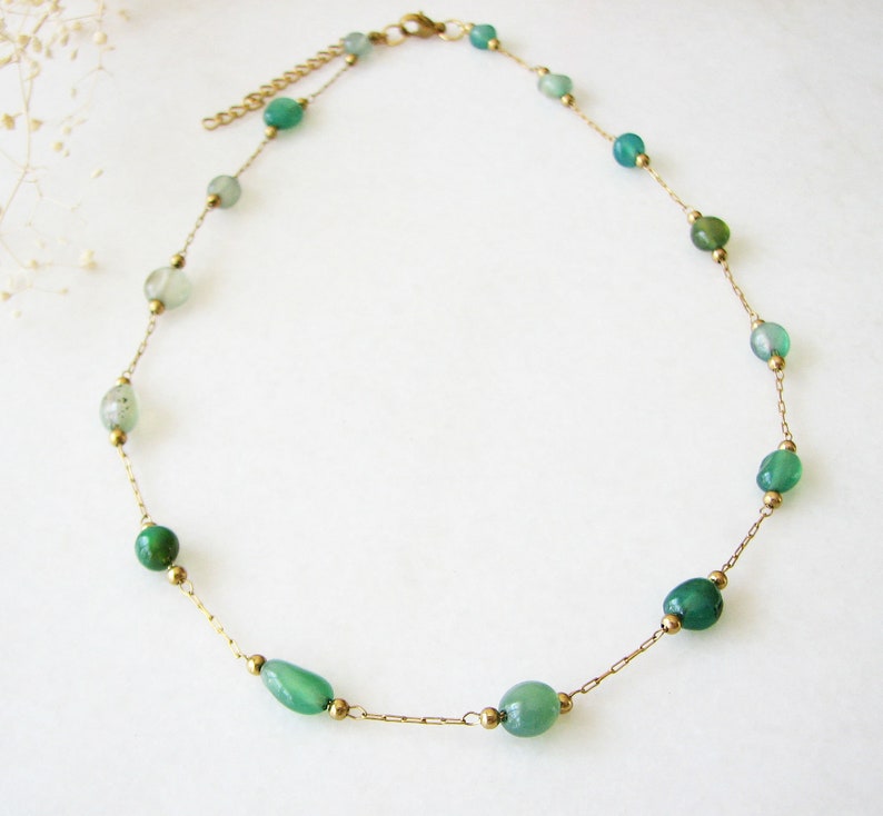 Puede incluir: Un collar de cadena dorada con cuentas de piedras preciosas verdes. El collar es delicado y presenta una variedad de tonos verdes.