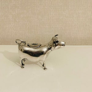 Può includere: Un lattiera in argento a forma di mucca con un coperchio incernierato. La mucca è in piedi su quattro zampe e presenta un design dettagliato.