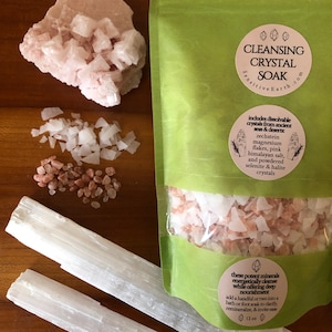 May include: A green pouch with a white label that reads "Cleansing Crystal Soak Sensitive Earth.com". The pouch contains a mixture of pink and white crystals. The label also includes a list of ingredients: "includes dissolvable crystals from ancient seas & deserts zechstein magnesium flakes, pink himalayan salt, and powdered selenite & halite crystals". There is a smaller white label that reads "these potent minerals energetically cleanse while offering deep nourishment add a handful or two into a bath or foot soak to clarify, remineralize, & invite ease 12 oz".