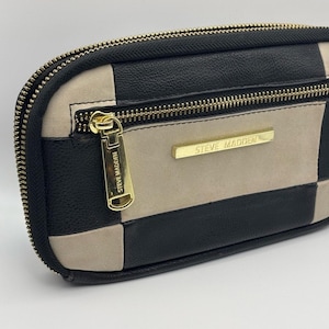 May include: A rectangular Steve Madden wallet featuring a black and beige checkered pattern. The wallet has a gold-tone zipper closure and a gold metal logo plate on the front. The zipper pull also features the Steve Madden brand name engraved.