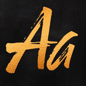 May include: Gold-colored letters "Aa" painted on a black background.