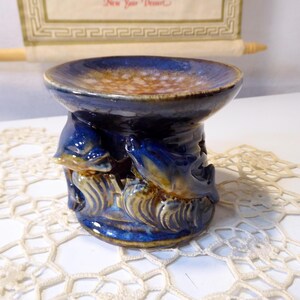 Op de afbeelding: Blauwe en bruine keramische oliebrander met een dolfijnendesign. De brander heeft een ronde bovenkant en een basis met drie dolfijnen.