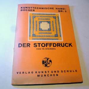 Op de afbeelding: Een vintage oranje boekomslag met de titel "Der Stoffdruck" van Th. Steinoel. De omslag heeft een geometrisch ontwerp in blauw, geel en zwart.