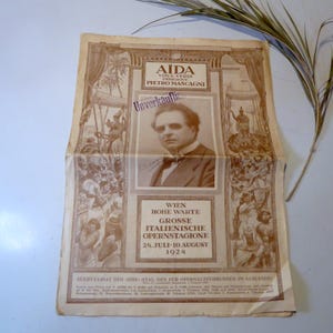 Pode incluir: Uma fotografia a preto e branco de um homem de fato e gravata. A fotografia está num anúncio de jornal antigo para uma apresentação de ópera de Aida de Giuseppe Verdi. O anúncio está em alemão e lista as datas da apresentação de 24 de julho a 10 de agosto de 1924.