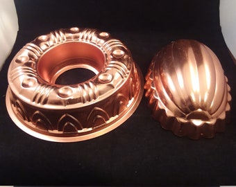 Puede incluir: Dos moldes para pasteles de cobre vintage. Uno es un molde de anillo con un diseño decorativo. El otro es un molde en forma de concha.