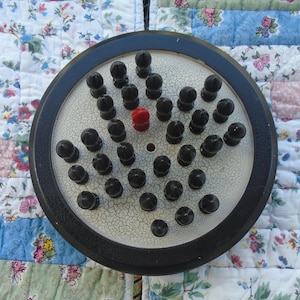 May include: A black and white game board with a red game piece in the center. The board has a cracked white surface and is surrounded by a black rim.