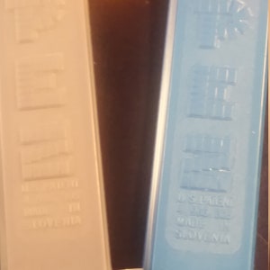 May include: Close-up of two PEZ dispensers. One is light beige, the other is light blue. Both have the PEZ logo and text that reads "U.S. Patent" and "Made in Slovenia".