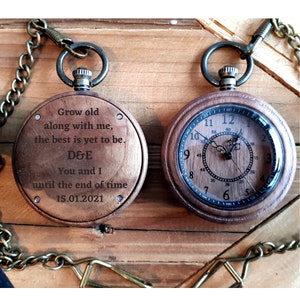 May include: A wooden pocket watch with a gold chain. The watch face has a black background with white numbers and hands. The back of the watch has an engraved message: "Grow old along with me, the best is yet to be. D&E You and I until the end of time 15.01.2021"