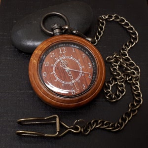 May include: A wooden pocket watch with a brown face and a silver chain. The watch face has Roman numerals and a second hand.