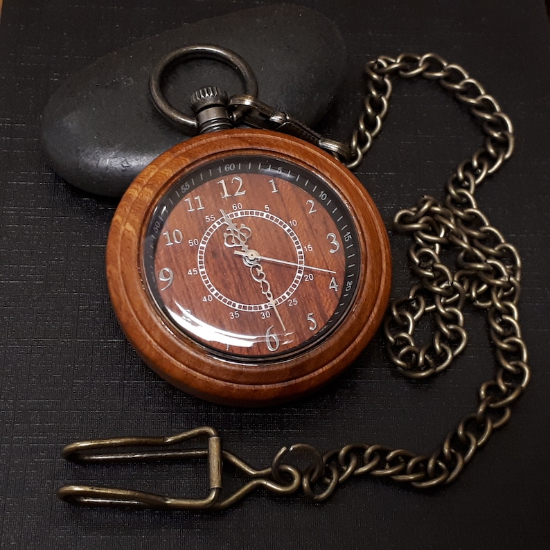 May include: A wooden pocket watch with a brown face and a silver chain. The watch face has Roman numerals and a second hand.