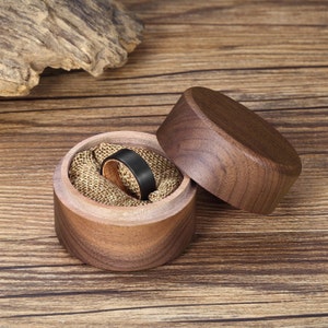 May include: A black and brown wooden ring in a walnut wood ring box. The ring is made of tungsten carbide and has a black finish. The box is made of walnut wood and has a natural finish.