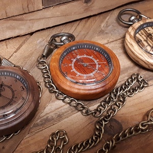 May include: Three wooden pocket watches with brass chains. The watches have different wood grain patterns and each has a different face design.