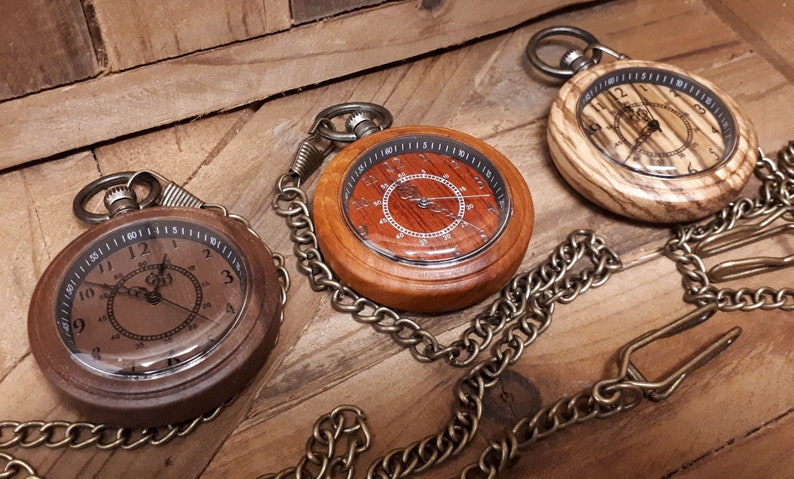 May include: Three wooden pocket watches with brass chains. The watches have different wood grain patterns and each has a different face design.