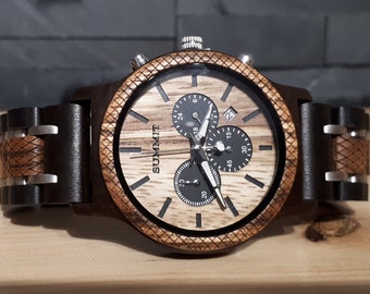 May include: A wooden wristwatch featuring a light brown wood grain dial with the word SUMMIT printed in black. The watch includes three black sub-dials, a date window, and a textured brown wood bezel. The band consists of dark brown wood links.