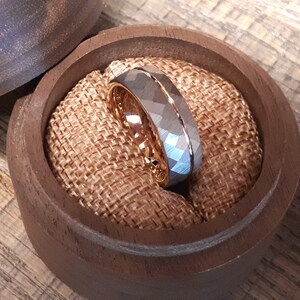 May include: A silver and rose gold wedding band with a hammered finish. The ring is displayed in a wooden ring box.