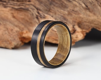 May include: A black and brown wooden ring with a black band and a brown wood inlay. The ring is sitting on a wooden surface.