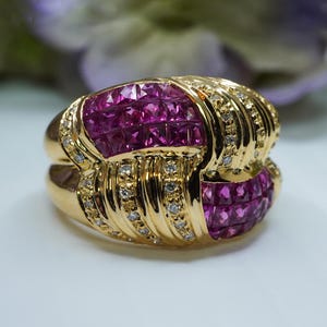 May include: A gold ring with a large pink ruby stone set in the center. The ruby is surrounded by smaller diamonds. The ring is a statement piece and would be perfect for a special occasion.