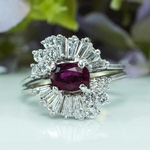 Puede incluir: Un anillo con un gran rubí ovalado rodeado por un halo de diamantes más pequeños. Los diamantes están engastados en un delicado diseño floral.