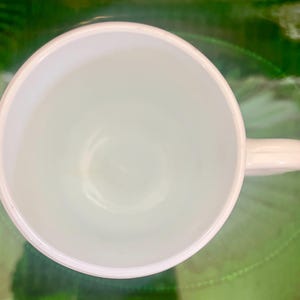 Op de afbeelding: Een witte keramische mok met een handvat. De mok is leeg en heeft een gladde, glanzende afwerking.