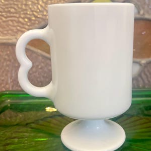 Op de afbeelding: Witte keramische mok met een hartvormig handvat en een voet.