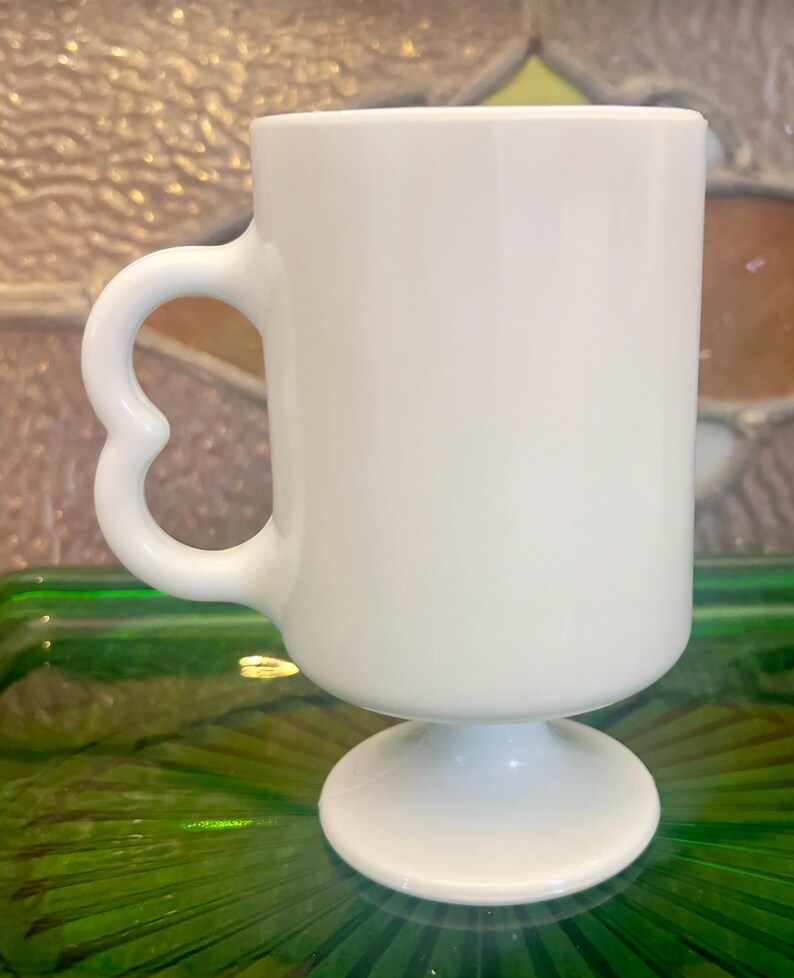 Op de afbeelding: Witte keramische mok met een hartvormig handvat en een voet.