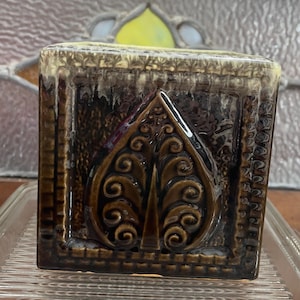 May include: Square ceramic planter with a brown and green glaze. The planter features a raised design of a stylised leaf in the centre.