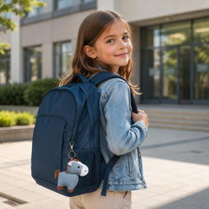 Könnte beinhalten: Ein einfarbiger marineblauer Rucksack mit einer seitlichen Netztasche und einem kleinen Plüschpferd-Schlüsselanhänger am vorderen Reißverschluss. Der Rucksack verfügt über verstellbare Schultergurte und ein Hauptfach mit Reißverschluss.