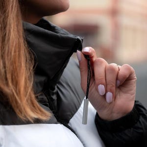 Puede incluir: Primer plano de una chaqueta acolchada en blanco y negro con un tirador de cremallera de metal plateado. La chaqueta tiene un cuello alto y un cordón. El cordón es negro con un patrón blanco.