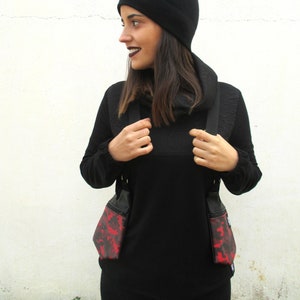 May include: A person wearing a black mock neck shirt with a black beanie and a red and black camouflage print crossbody bag.