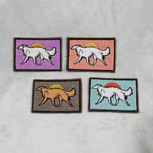 May include: Four embroidered patches featuring a dog silhouette with a setting sun design. Each patch has a different background color: purple, peach, brown, and teal. The dog is white, and the sun is orange.