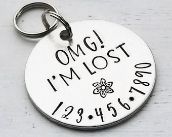 May include: Silver dog tag with the text "OMG! I'M LOST" and a small flower design. The tag also has the numbers 1, 2, 3, 4, 5, 6, 7, 8, 9, 0 around the edge.