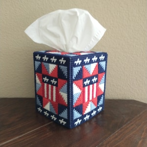 May include: A blue, red, and white tissue box cover with a star and stripe pattern. The cover is made of plastic canvas and is decorated with a patriotic theme.