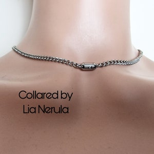 May include: A silver chain necklace with a magnetic clasp. The necklace is on a mannequin's neck. The text "Collared by Lia Nerula" is printed below the necklace.