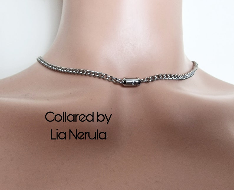 May include: A silver chain necklace with a magnetic clasp. The necklace is on a mannequin's neck. The text "Collared by Lia Nerula" is printed below the necklace.