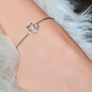 May include: A silver chain bracelet with a charm featuring two cats inside a heart.