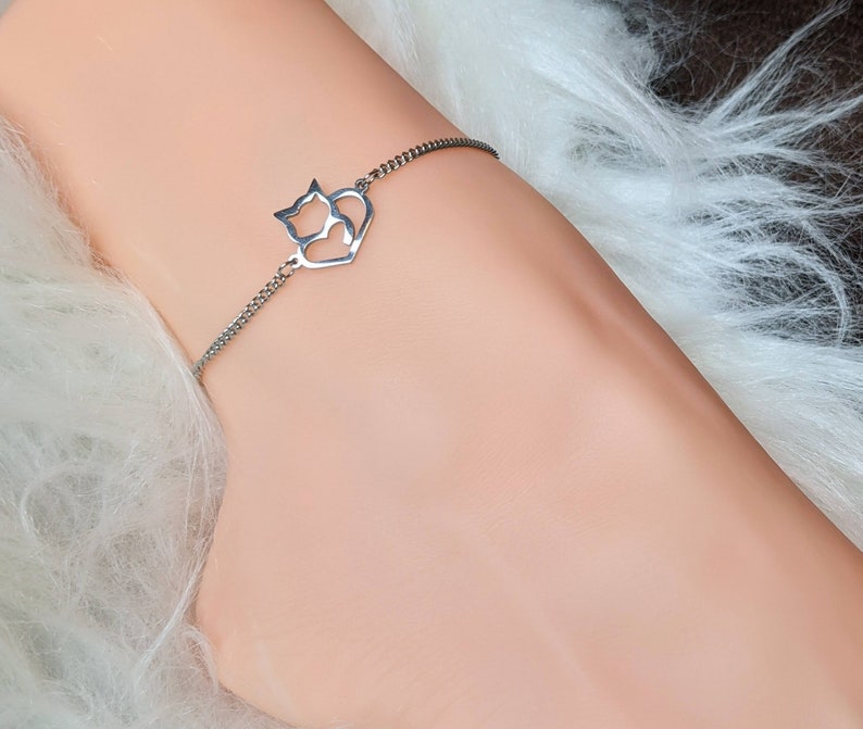 May include: A silver chain bracelet with a charm featuring two cats inside a heart.