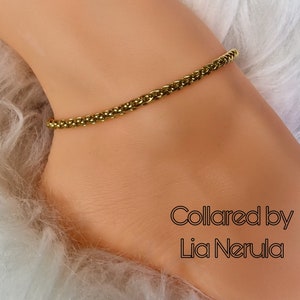 May include: A gold chain ankle bracelet on a white fuzzy surface. The text "Collared by Lia Nerula" is visible below the bracelet.