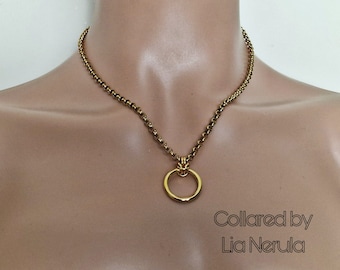 May include: A gold-colored necklace with a circular pendant. The necklace has a chain-like design with small, round beads. The pendant is a simple, open circle. The text "Collared by Lia Nerula" is visible in the image.